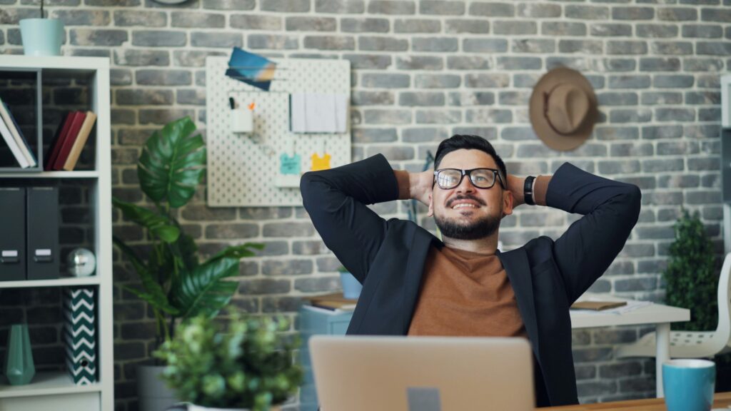 uomo al pc con le mai dietro la testa e viso sorridente